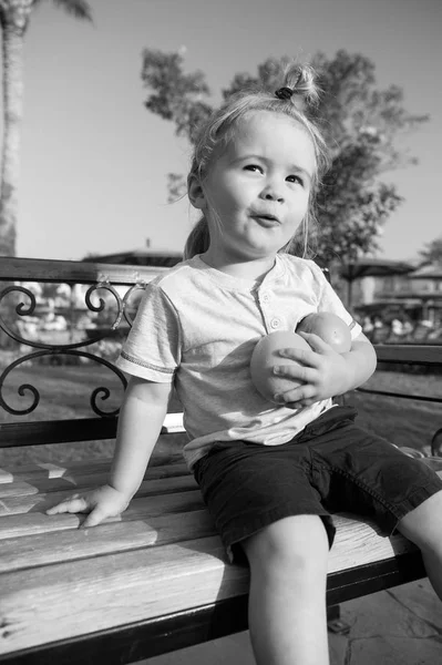 Дитина сидить з двома апельсинами на лавці — стокове фото