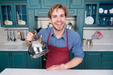 Mavi gömlek, kırmızı önlük gülümseme su ısıtıcısı ile adam yemek