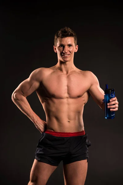 Homem atleta com garrafa de esporte no fundo escuro — Fotografia de Stock