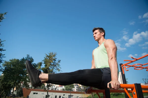 Deportista mantenga las piernas levantadas rectas en barras paralelas, entrenamiento — Foto de Stock