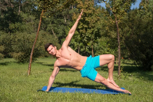 Спортсмен растягивает руки и ноги на синем коврике в парке — стоковое фото