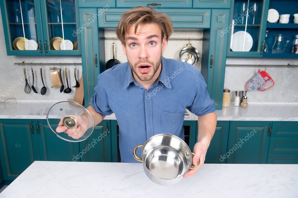 Guy with surprised face hold open saucepan, lid in kitchen