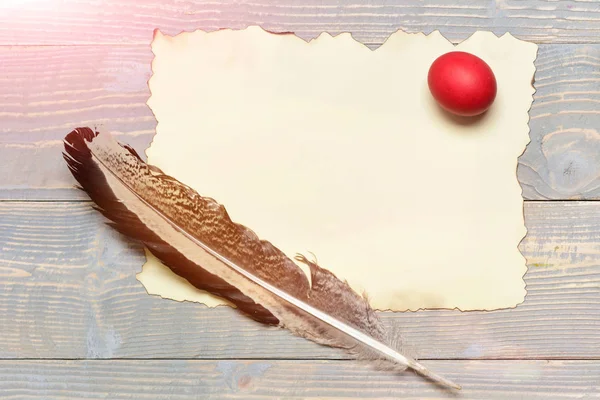 red easter egg with writing feather and paper on wood