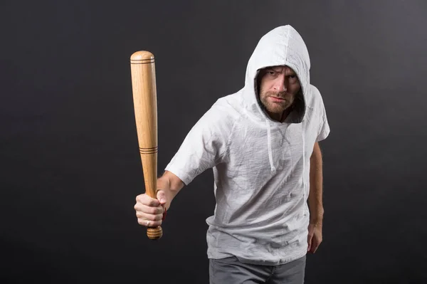 Man hold baseball bat, agression. Hooligan wear hood in hoody, fashion. Gangster guy threaten with bat weapon. Aggression, anger and violence concept