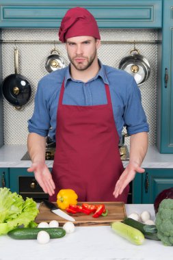 Yemek pişirmek için gerekli malzemeler. Adam masadaki sebzeleri işaret ediyor. Mutfakta aşçı şapkası ve önlüğü var. Vejetaryen menüsü ve sağlıklı beslenme. Yemek hazırlama ve yemek tarifleri