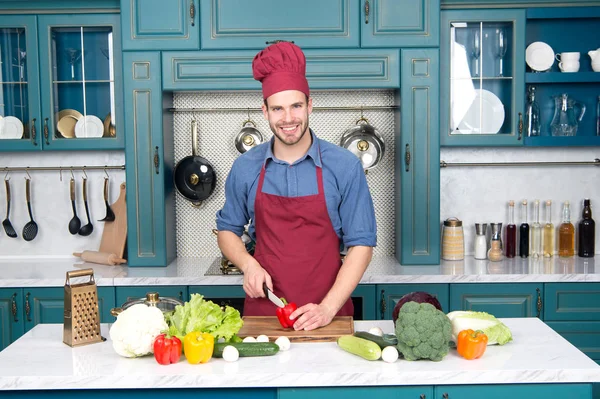 Sorrindo jovem cortando legumes na cozinha — Fotografia de Stock