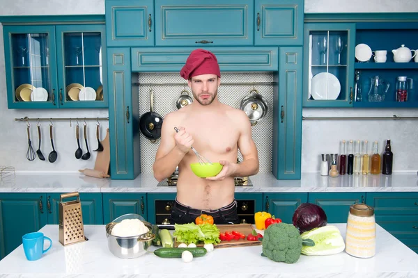 Uomo tenere ciotola e frullare a tavola. Chef con busto muscoloso cuoco in cucina. Verdure e utensili per cucinare i piatti. Preparazione del cibo e ricette di cottura. Menù vegetariano e dieta sana — Foto Stock