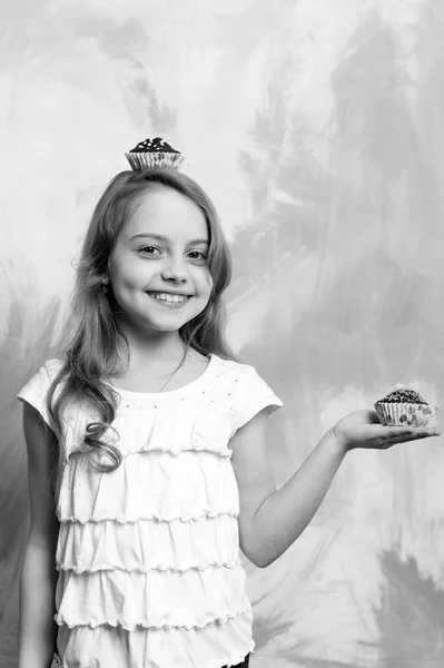 Mädchen lächelt mit Cupcakes in der Hand und auf dem Kopf — Stockfoto