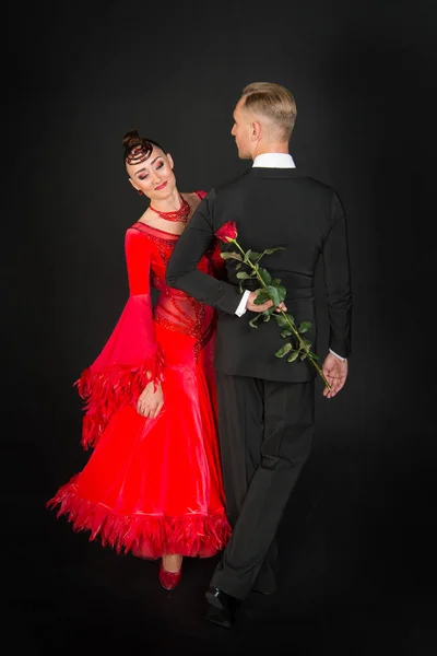 Sensual woman and man dance with rose flower. Woman in red dress and macho in tuxedo. Couple of ballroom dancers in love. Valentines day celebration. Love proposal and date concept