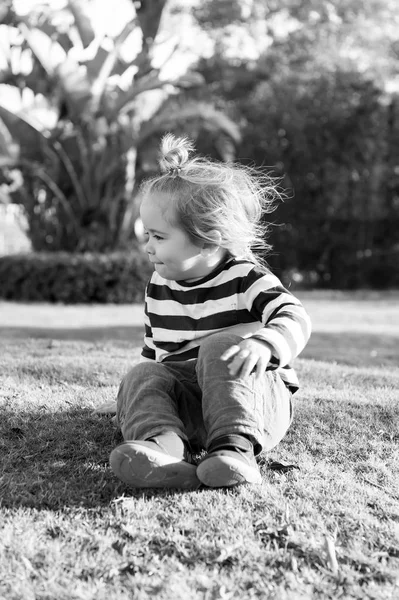 Niño con el pelo rubio en ropa azul sentarse en la hierba —  Fotos de Stock