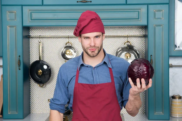 Чоловік тримає фіолетову капусту на кухні. Готується в шапці для шеф-кухарів і фартусі. Овочі та кухні для приготування страв. Вегетаріанське меню і здорова дієта. Рецепти приготування їжі та приготування їжі — стокове фото