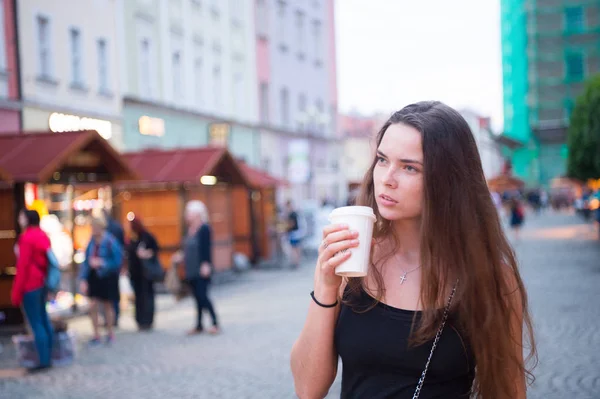 Женщина с выпивкой на вынос ходит по улице. Женщина держит одноразовую чашку кофе. Кофе или чай настроение. Напитки и еда во время летних каникул или путешествий. Девушка с длинными волосами и натуральным макияжем — стоковое фото