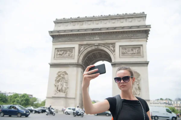 Γυναίκα με smartphone σε αψίδα μνημείο στο Παρίσι, Γαλλία. Γυναίκα κάνει selfie με το τηλέφωνο στο arc de triomphe. Διακοπές και αξιοθέατα στη γαλλική πρωτεύουσα. Κορίτσι με εμφάνιση μόδας και αισθησιακή ομορφιά — Φωτογραφία Αρχείου