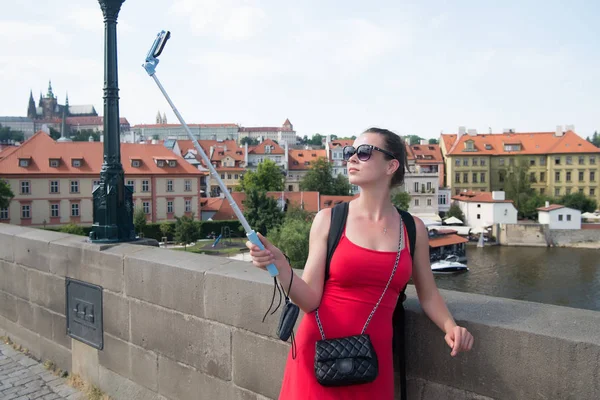 Γυναίκα βγάζει selfie με κινητό τηλέφωνο στην Πράγα, Τσεχία. Γυναίκα με smartphone στο ραβδί στη γέφυρα πάνω από το ποτάμι. Κορίτσι τουρίστρια με εμφάνιση μόδας και αισθησιακή ομορφιά. Ταξίδια και αξιοθέατα της πόλης — Φωτογραφία Αρχείου