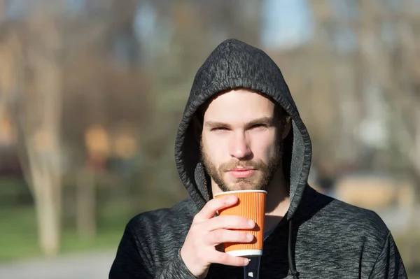 Hombre barbudo con bebida para llevar en Sunny Park. Macho en la capucha sostener taza de café desechable. Café o té. Bebida y comida al aire libre. Té de la mañana para el desayuno —  Fotos de Stock