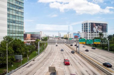 Miami, Amerika Birleşik Devletleri - 30 Ekim 2015: otoyol veya karayolu ile otomobil ve gökdelenler bulutlu mavi gökyüzü üzerinde. Taşıma/iş arabaları için trafik yol işaretleri. Binalar üzerinde reklam panoları. Genel alt yapı kavramı