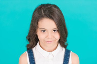 Uzun, sağlıklı esmer saçlı çocuk modeli gülümsemesi. Mavi arka planda genç yüzlü bir kız. Çocuk, çocukluk konsepti. Güzellik, bak, saç stili. Cilt bakımı, sağlık, gençlik, bodur pastel