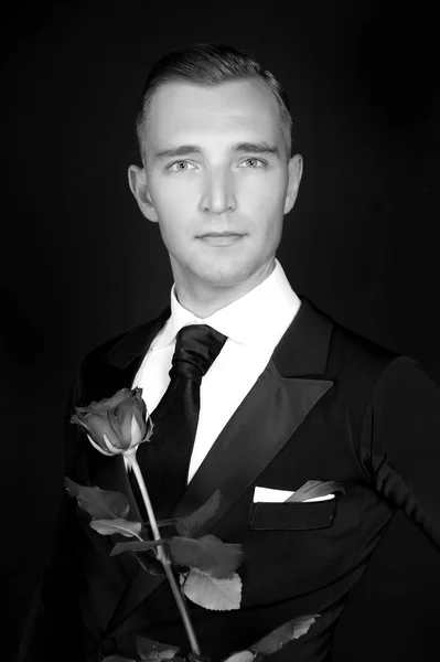 Black and white image of groom with flower in hands