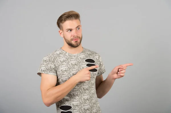 Hombre presentando producto sobre fondo gris. Macho con gesto de dedo barbudo en la cara. Presentación, anuncio, publicidad y concepto de promoción, espacio de copia — Foto de Stock