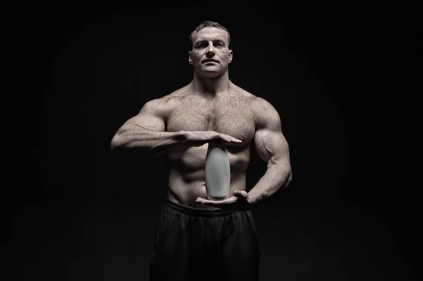 Bodycare and hygiene for sportsman. Bodybuilder hold shampoo or gel bottle. Man athlete with fit torso and ab. Spa bath or shower cosmetic after training in gym, vintage — Stockfoto