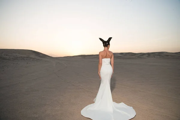 沙漠里穿婚纱的女人性感女人的黑发。新娘在白色礼服在日落天空, 后面看法。沙丘上的时装模特。美丽的女孩与魅力看 — 图库照片