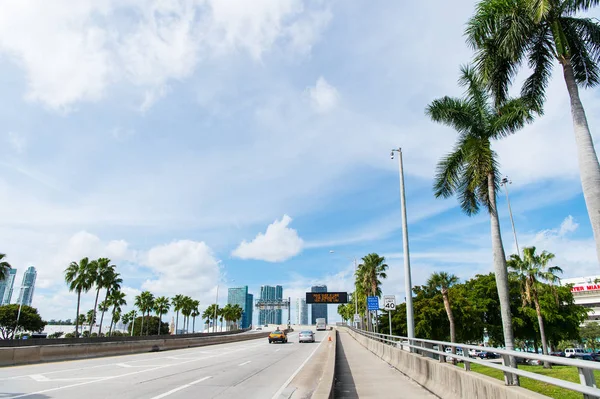 Autobahn oder Fahrbahn mit Autos und Skyline von miami, USA. Straße mit Verkehrsschildern für Transportfahrzeuge und Palmen am bewölkten blauen Himmel. Konzept der öffentlichen Infrastruktur. Anreise mit dem Auto — Stockfoto