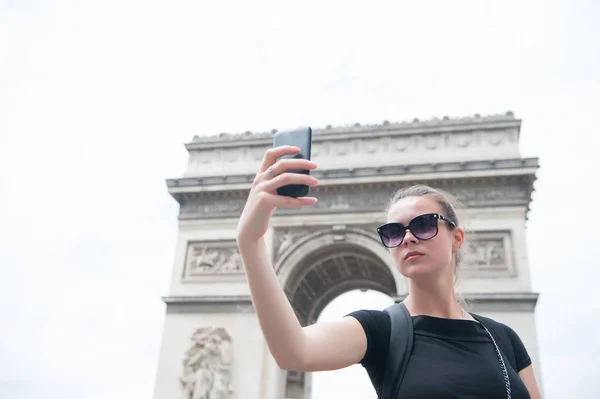 Γυναίκα κάνει selfie με το τηλέφωνο στο arc de triomphe στο Παρίσι, Γαλλία. Γυναίκα με smartphone στο μνημείο αψίδα. Διακοπές και αξιοθέατα στη γαλλική πρωτεύουσα. Κορίτσι με εμφάνιση μόδας και αισθησιακή ομορφιά — Φωτογραφία Αρχείου