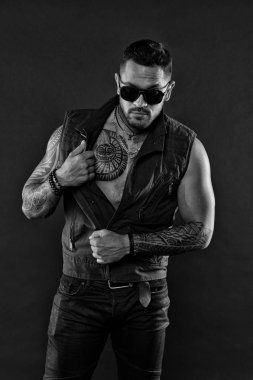 Moda giysiler dövmeli adam. Dövmeli kas maço. Moda modeli Güneş gözlüğü. Dövmeli adam ve sakal şık bir görünüm vardır. Son moda deri yelek, siyah ve beyaz spor sporcu