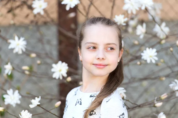 Frühjahrs-, Oster- und Feiertagskonzept. Kleines Mädchen auf Blumenblüte im Frühling. Kind mit blühenden Blumen im Freien. Schönheitskind mit frischem Look und langen Haaren — Stockfoto