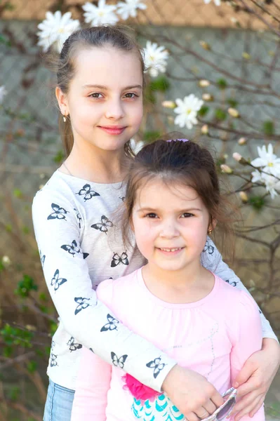 Niñas posan en flor floral en jardín de primavera. Las hermanas disfrutan de la primavera al aire libre. Niños con flores en flor. Concepto de familia, amor y confianza —  Fotos de Stock