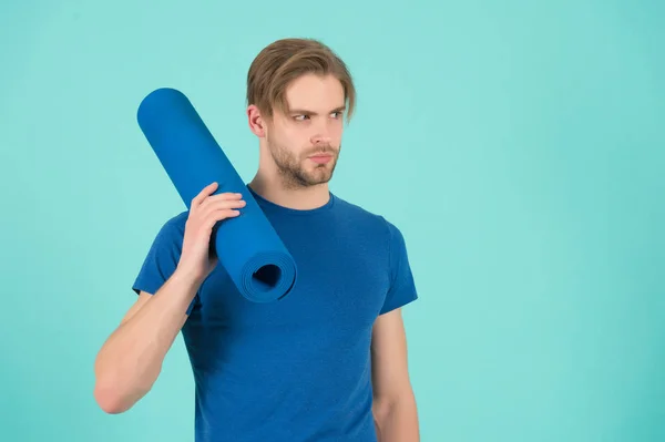 Sportsman tenir tapis de yoga. Athlète de mode en t-shirt bleu. Homme barbu aux cheveux élégants. Équipement de gymnastique pour l'entraînement et l'entraînement. Yoga sportif et pilates activité, espace de copie — Photo