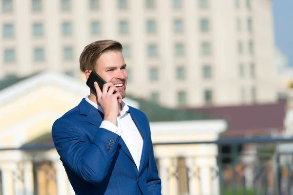 Comunicación empresarial y nuevas tecnologías. Feliz hombre de negocios con smartphone en terraza soleada. Hombre sonrisa en traje formal con teléfono móvil al aire libre. Concepto de estilo de vida — Foto de Stock