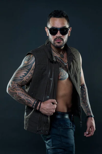 Tattoo model with beard and glasses on unshaven face. Macho with tattoo on strong arm. Tattooed muscular man in trendy clothes. Fashion athlete with confidence and charisma. Fashion style and trend