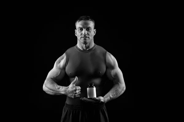 Nahrungsergänzungsmittel für Bodybuilder. Sportler mit Vitaminflasche zeigen Daumen hoch. Nahrung und Ernährung für Sport und Fitness. Energie- und Wellness-Konzept, schwarz-weiß — Stockfoto