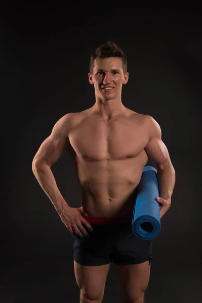 Sonrisa deportiva con torso sexy y paquete de seis. El hombre feliz sostiene la esterilla de yoga. Atleta sonriendo con fuertes brazos en pantalones cortos. Equipo de gimnasia para entrenamiento y entrenamiento. Yoga deportivo y actividad física —  Fotos de Stock