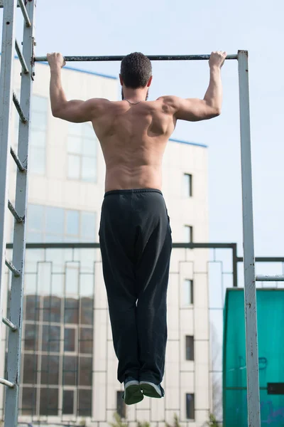 Man do chin ups outdoor. Sportsman pull up on stadium. Athlete with fit torso and strong hands on bar. Chin up bar exercises. Workout and training activity. Strength or power and sport, back view