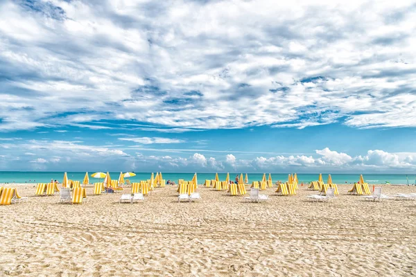 Sillas de playa y sombrillas en el cielo nublado en miami, EE.UU. Playa de mar con arena blanca y agua azul en un día soleado. Vacaciones de verano en el mar o el océano. Wanderlust o viajar y aventura — Foto de Stock