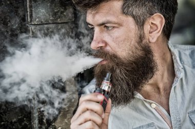 Sakallı adam vape, beyaz bulutlar duman sigara içiyor. Elektronik sigara kavramı. Uzun sakallı adam rahat görünüyor. Adam sakal ve bıyık sakin yüz, koyu arka plan, defocused