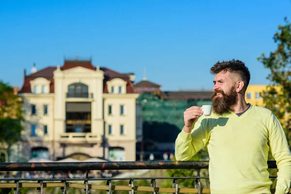 Homme à longue barbe profiter du café. Concept rituel du matin. Homme barbu avec une petite tasse, boit du café. Homme avec barbe et moustache sur le visage souriant boit du café au balcon, fond urbain, déconcentré — Photo