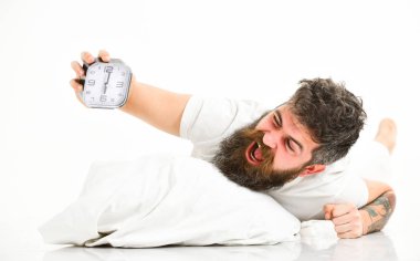 Bağıran yüzlü bir adam çalar saatin yanında, yastığın üzerinde yatıyor..