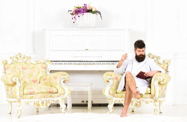 Junger Geschäftsmann genießt seinen morgendlichen Kaffee vor der Arbeit. Konzentrierter Typ, der im Sessel ein Buch liest. Morgen im Hotel — Stockfoto