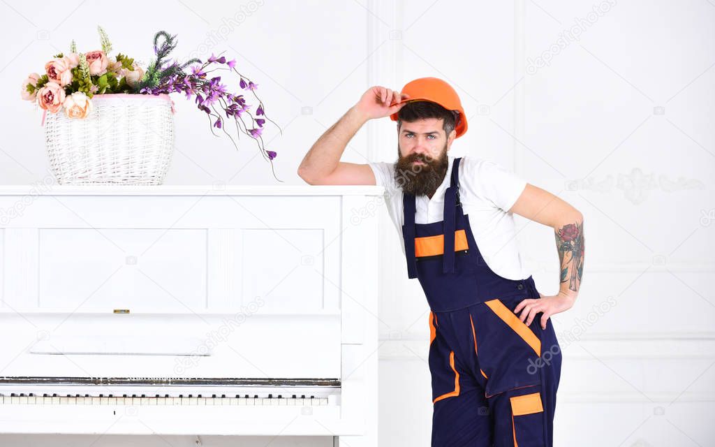 Handsome bearded mover posing next to retro piano isolated on white background. Small break from tiresome work