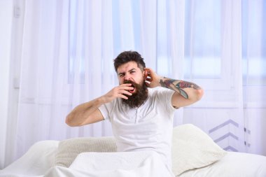 Yatak, beyaz perde arka plan üzerinde oturup sırasında esneme tişörtlü adam. Uykulu yorgun yüz esneme üzerinde adam. Uykucu kavramı. Maço sakal ve bıyık esneme, rahatlatıcı, nap, sahip rest