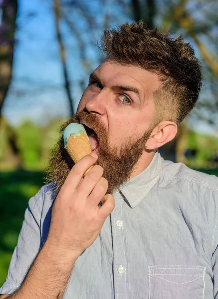 Concept de refroidissement. Homme à la barbe longue refroidissant avec un cône de crème glacée par une journée chaude ensoleillée, fermer. Homme avec barbe et moustache sur le visage grimace strict mange de la crème glacée, fond nature, déconcentré — Photo