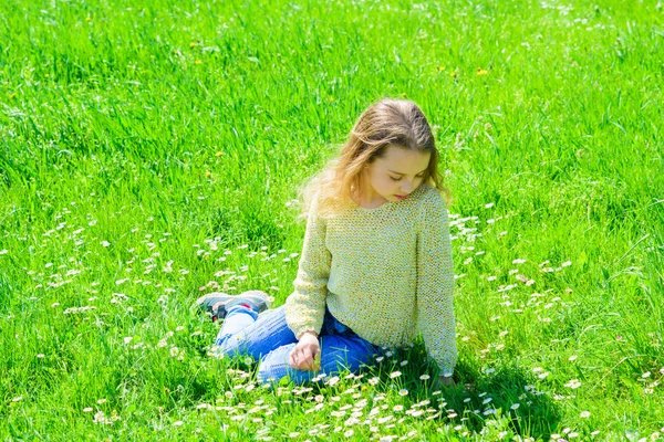 Sakin ya da üzgün yüz kız açık havada eğlence harcamak. Kız grassplot, arka planı yeşil çimlere oturur. Çocuk çayır otururken bahar güneşli hava keyfini çıkarın. Bahar kavramı — Stok fotoğraf