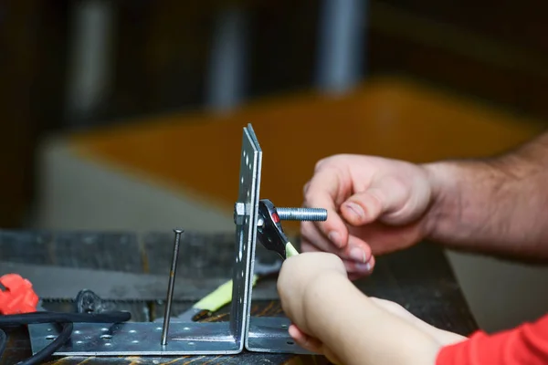 Repair and assistance concept. Childs hand helps adult to twist hex bolt. Father and son repairing together, close up. Male and childrens hands connecting metal plates, parts with hex bolt — Stock Photo, Image