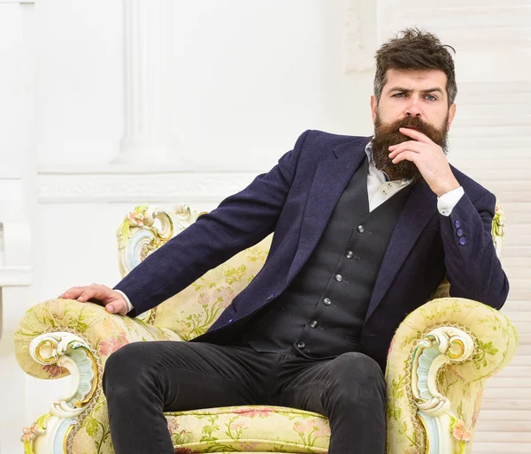 Macho atractivo y elegante en cara seria y expresión reflexiva. Hombre con barba y bigote con traje clásico, se sienta en un sillón a la antigua, fondo blanco. Elite concepto de estilo de vida —  Fotos de Stock