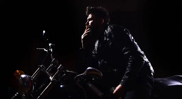 Natt racer koncept. Mannen med skägg, biker i skinnjacka sitter på motorcykel i mörker, svart bakgrund. Macho, brutal biker i läder jacka Rider motorcykel nattetid, kopia utrymme — Stockfoto
