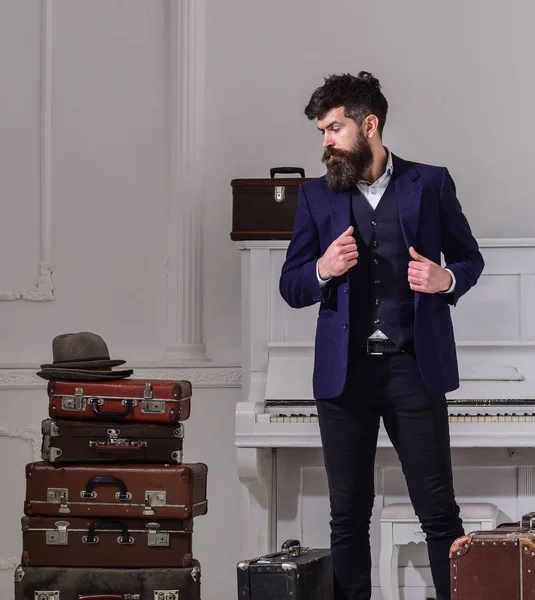 Macho-Styling auf nachdenklichem Gesicht, das neben einem Stapel Vintage-Koffer steht. Mann, Reisender mit Bart und Schnurrbart mit Gepäck, luxuriöser weißer Innenraum. Reise- und Gepäckkonzept — Stockfoto