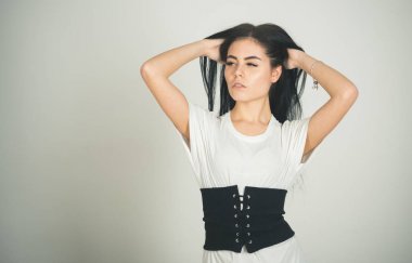 Gizemli dalgın yüz poz üzerinde beyaz kadın duvar arka plan üzerinde. Geniş siyah kemer bel üzerinde ile şık elbiseli Bayan. Kız esmer oyun uzun saçlı, kopya alanı. Saç bakım kavramı